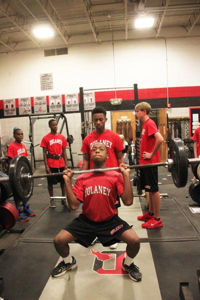 Sophomore Noah Squire-Rogers, senior eric williams and sophomores David Fulgham and Bobby Mulreaney watch as sophomore Aaron Holliday performs a power clean lift during his his period four weight training class.