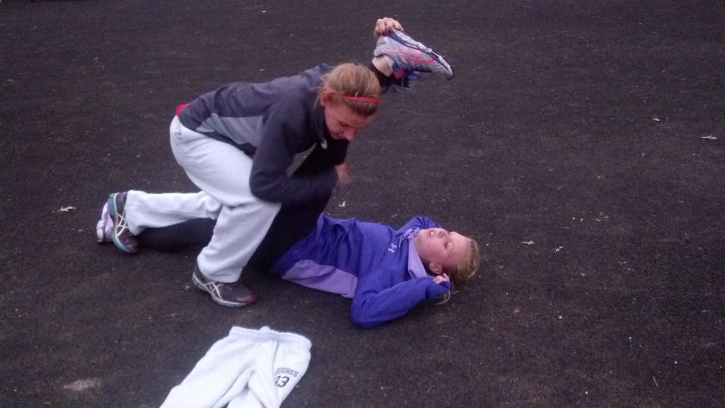 Sophomore Kristin Meek helps sister Freshman Jessica Meek stretch before practice.