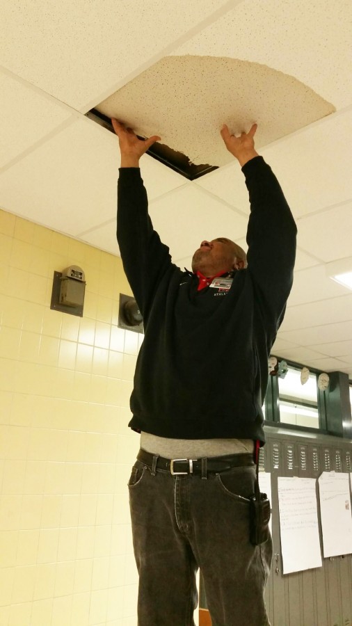 Custodian Derek Williams removes a ceiling tile drenched by  a valve break outside room 109 during period 2A March 9. Later, he hung a bucket under the leaky pipe to collect water. 