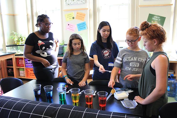 Senior Allie Ng (center) makes sugar rainbows by pouring sugar into multicolored glasses of water with middle school students at the Baltimore Montessori Public Charter School Oct. 17. The experiment demonstrated density by varying the amount of sugar in each glass.
